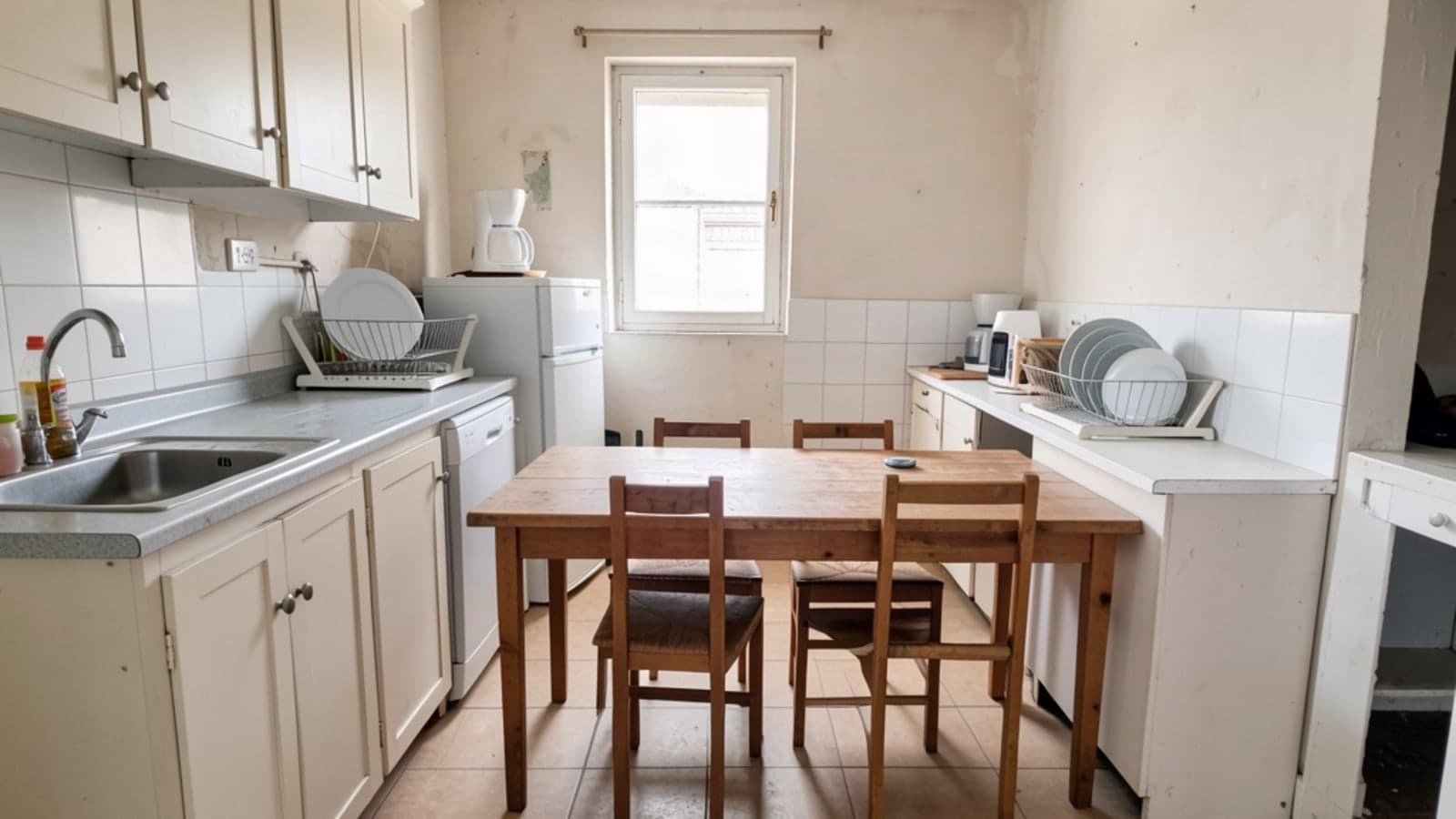 Shared kitchen with a wooden table and chairs, a dish rack on the counter, a fridge and a window